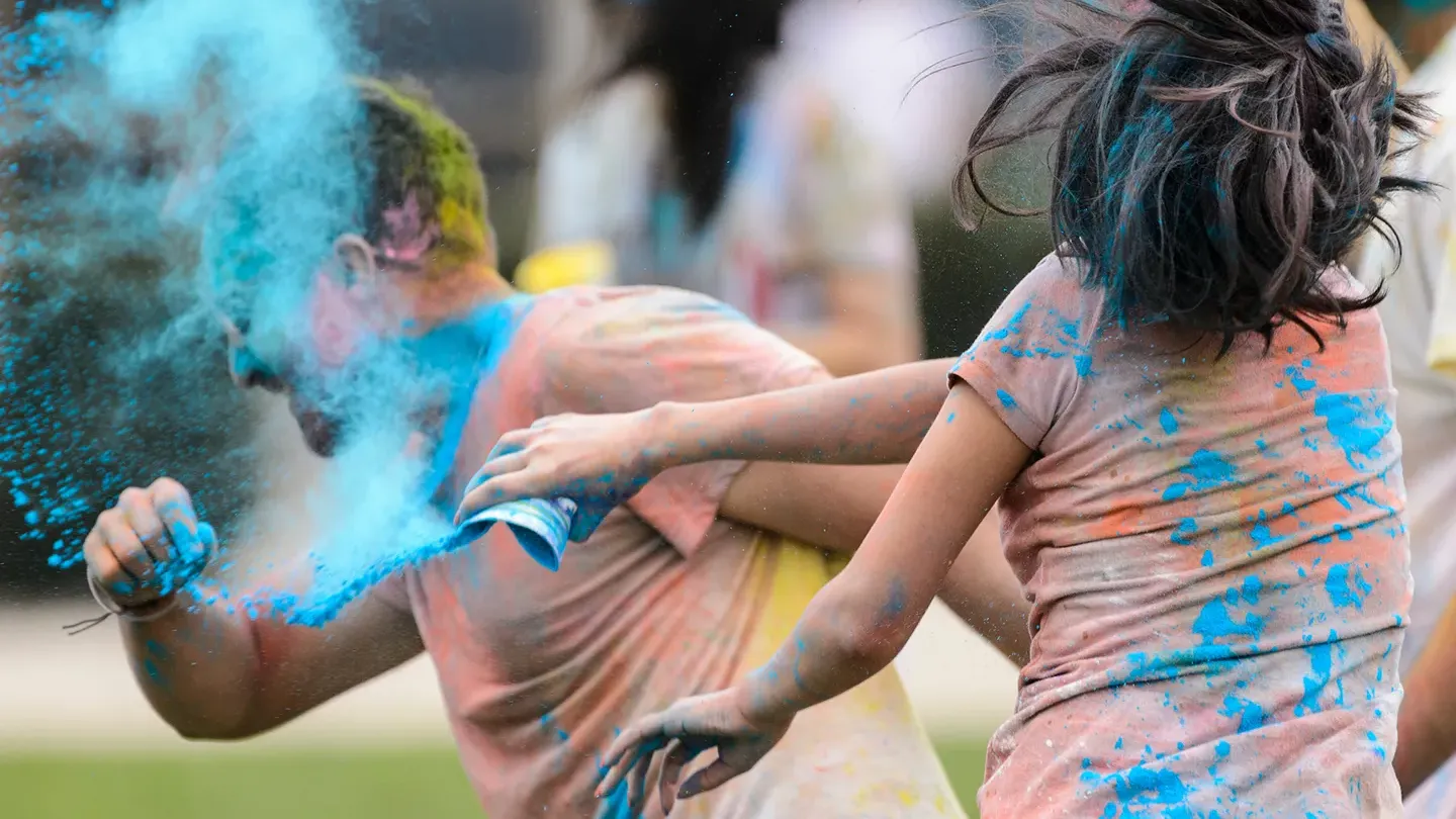 Action shot of two students spraying each other with blue powder as part of the UW–Madison Holi Color Fest