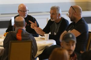 A man gestures while talking as three people listen at a table.