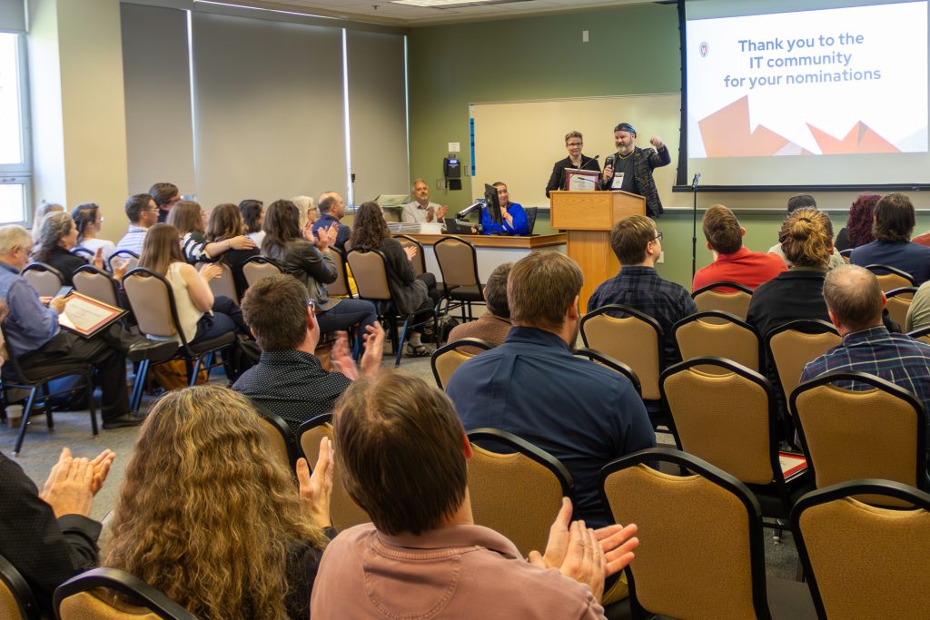 A seated audience claps for a person at the front of the room.