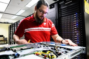 A man works with tools on a server rack in a server room