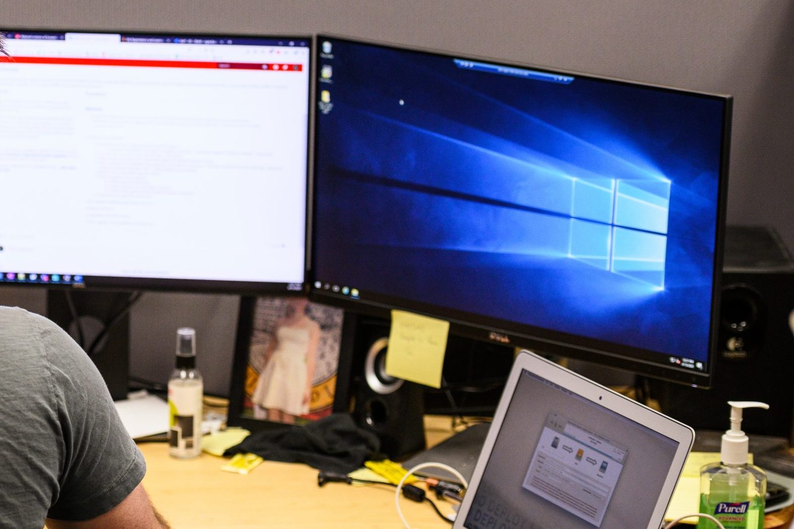 A person works at a desk with two monitors and a laptop computer