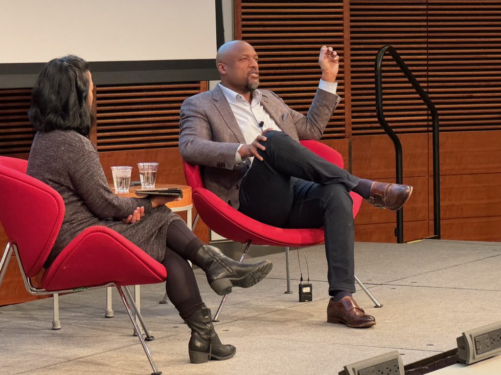 Two people sitting in chairs talking on a stage.