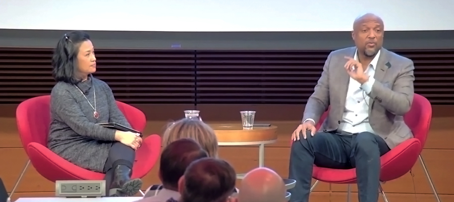 Two people sitting in red chairs in front of an audience.