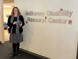 Maria Dahman stands next to a McBurney Disability Resource Center sign
